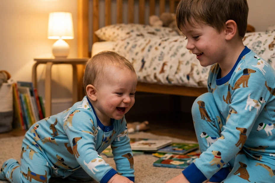 Two toddlers wearing matching light blue pajamas with a dog print are playing on a carpeted floor in a cozy bedroom setting.