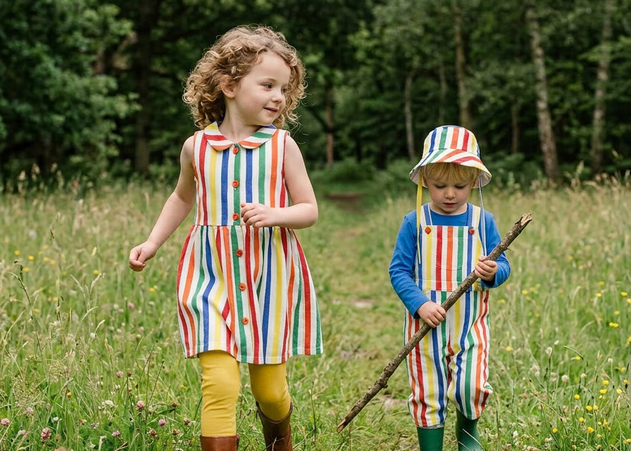 Two children in colorful outfits walking through a grassy field with trees in the background.