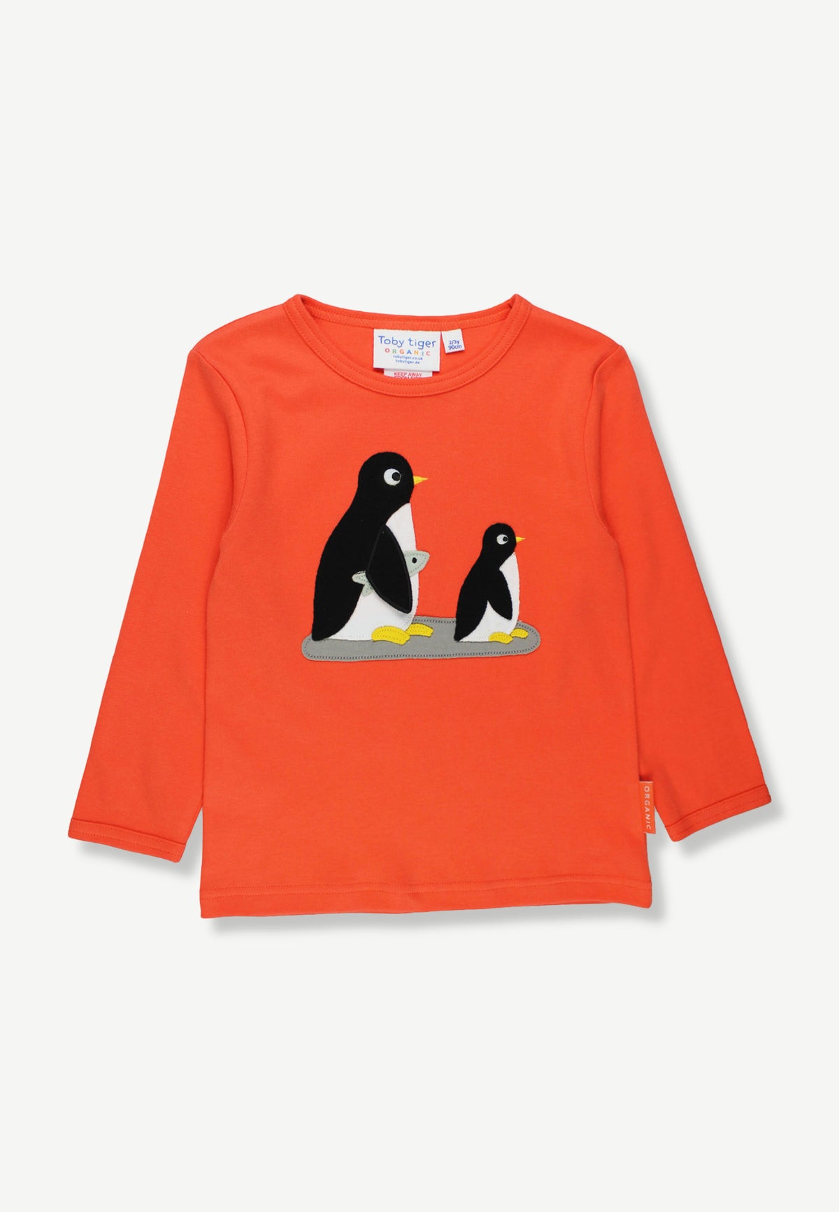 A bright orange long-sleeve children's top featuring a graphic of two penguins on the chest, displayed flat against a light off-white background.