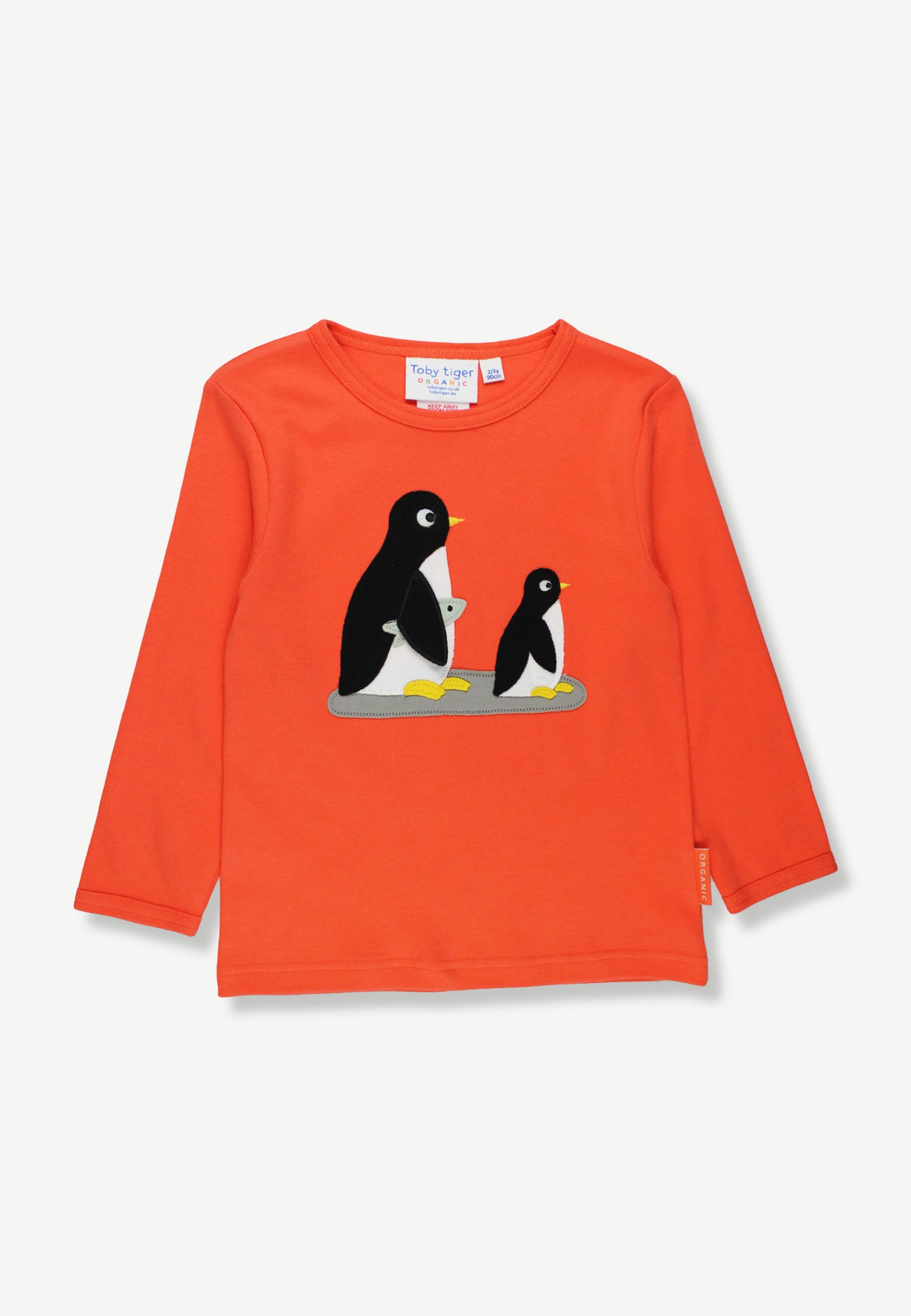 A bright orange long-sleeve children's top featuring a graphic of two penguins on the chest, displayed flat against a light off-white background.