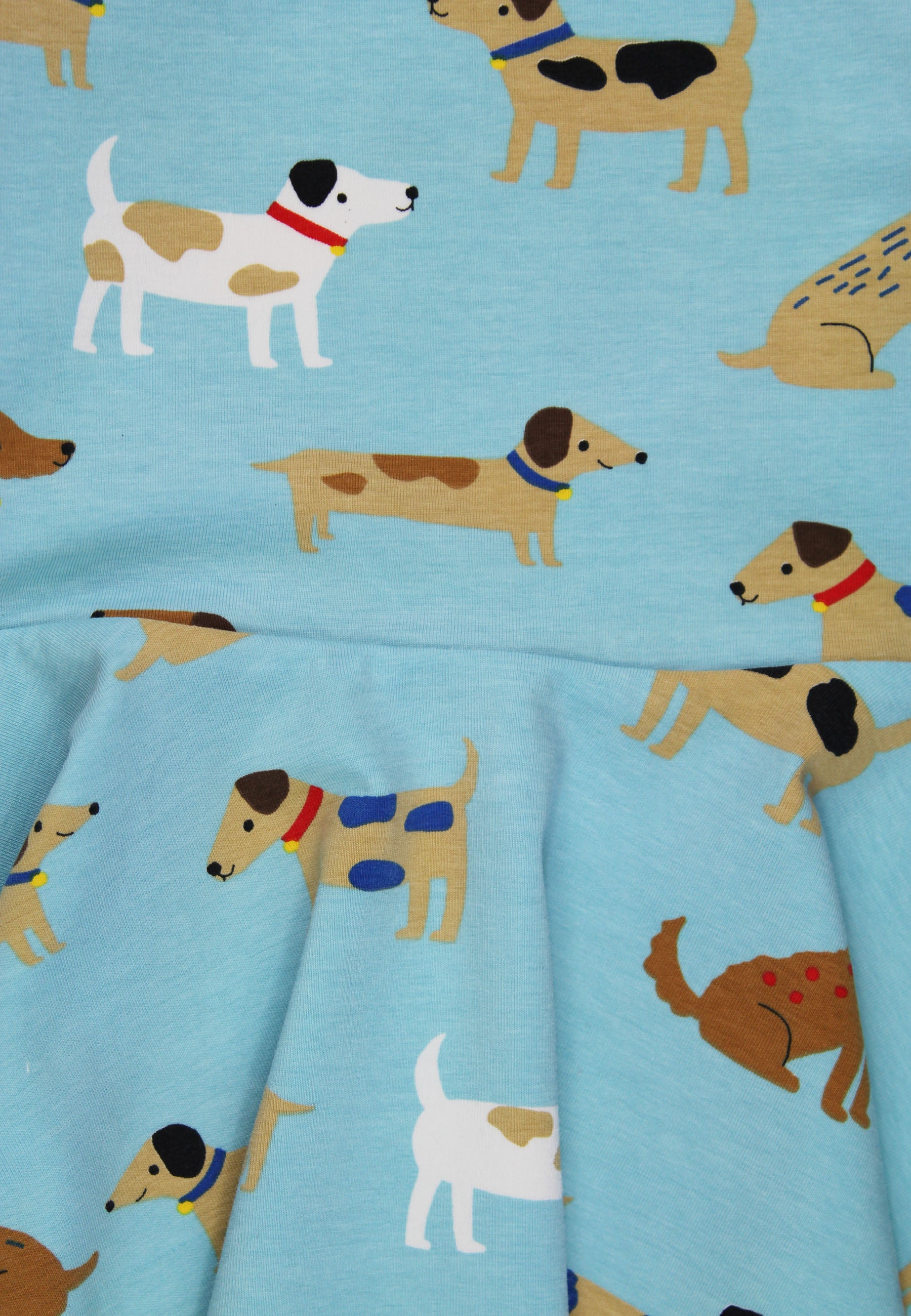 A close-up of a light blue fabric printed with cartoon dogs in tan, brown, white, black, red, and blue, with a gathered seam visible across the middle.