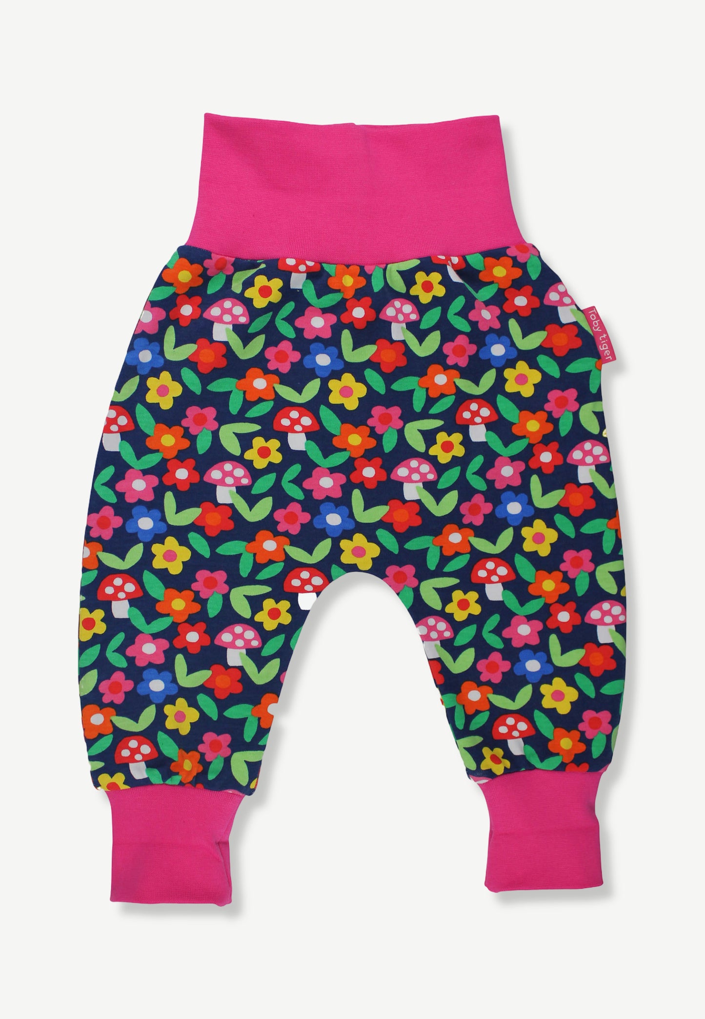 A pair of baby jogger pants featuring a colorful floral and mushroom print on a navy blue background, with bright pink elastic waistband and leg cuffs.