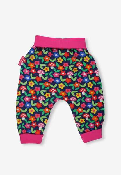 A pair of toddler's jogger pants featuring a colorful mushroom and flower pattern on a dark navy background, with bright pink elastic waistband and cuffs, shown against a light gray background.