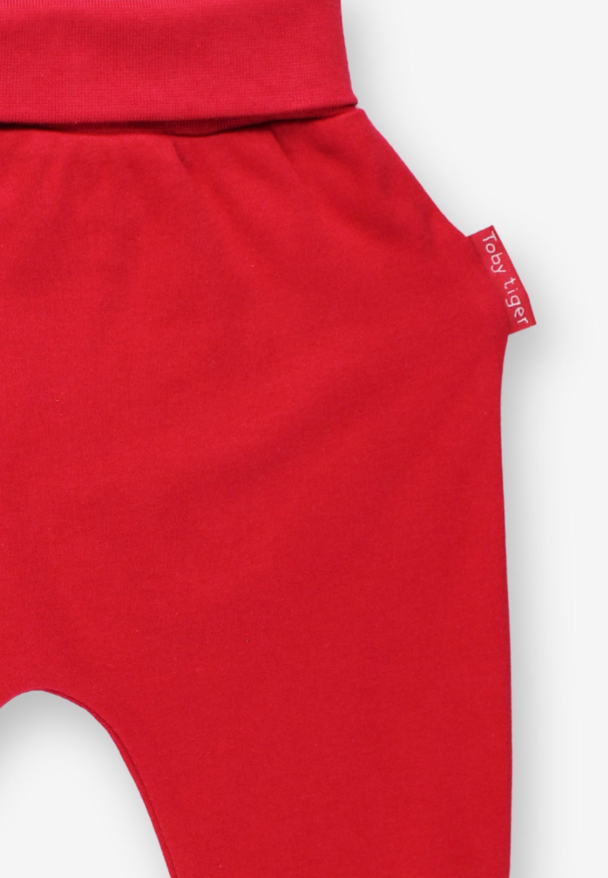 Close-up of bright red baby pants with a small side tag reading baby jagger, shown against a light neutral background.