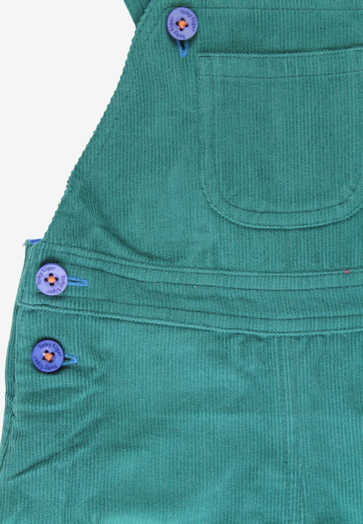 Close-up of a green corduroy garment, likely a pinafore or bib, showing a front pocket and purple decorative buttons with small orange and yellow centers.