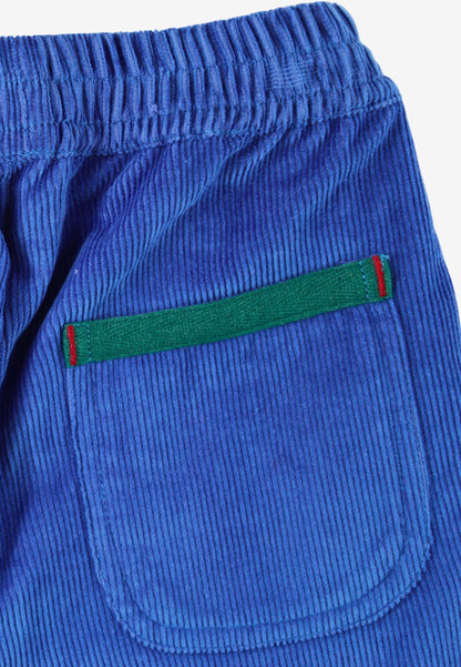 Close-up of blue corduroy trousers showing a back pocket with a green stripe detail bordered in red, on a white background.