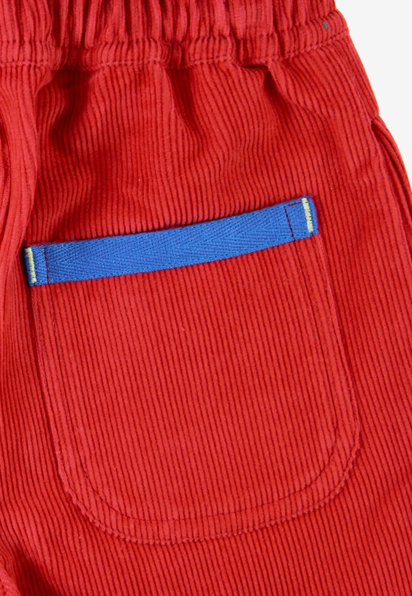 Close-up of red corduroy pants showing a front pocket with a blue fabric trim accent.