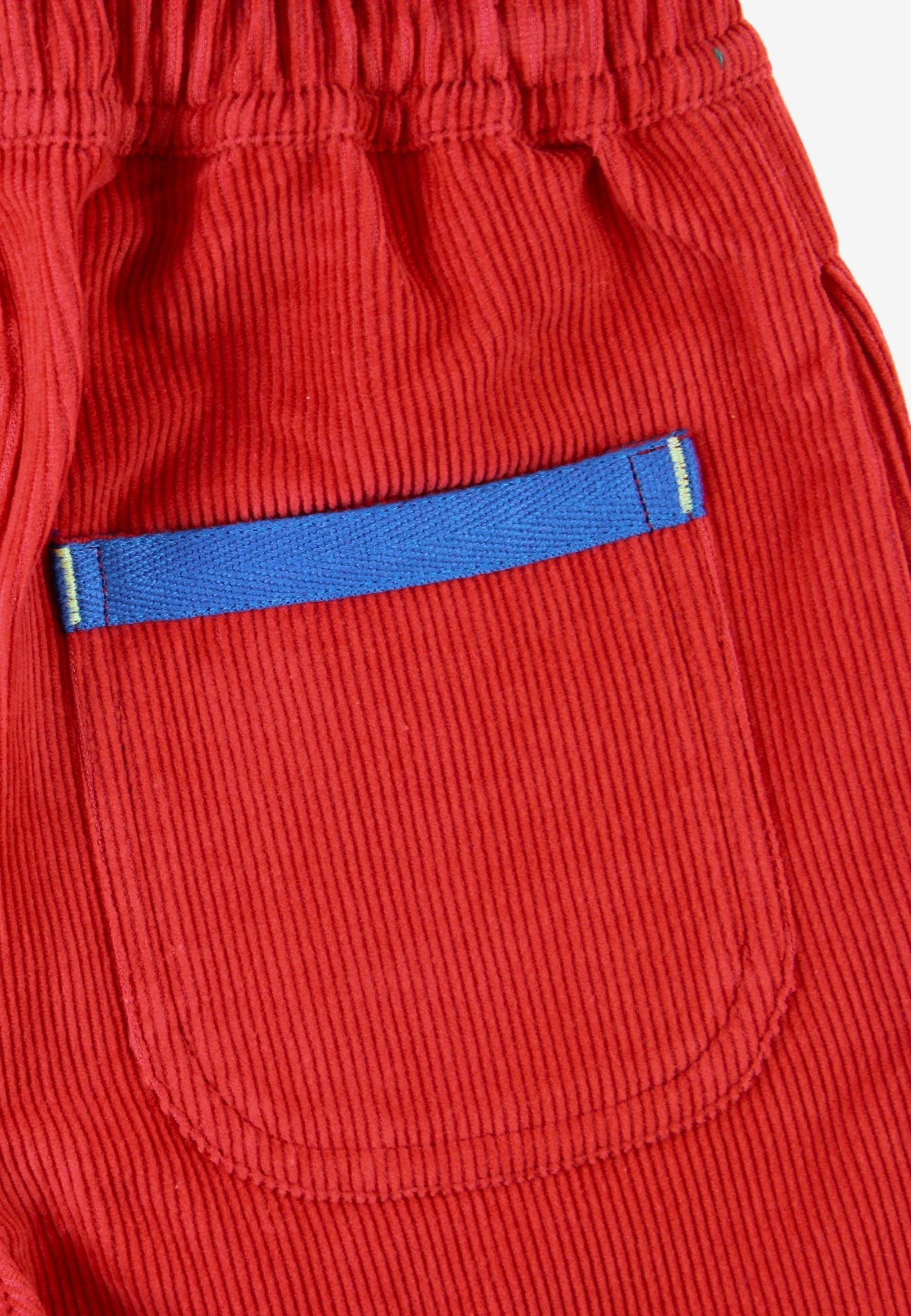 Close-up of red corduroy pants showing a front pocket with a blue fabric trim accent.