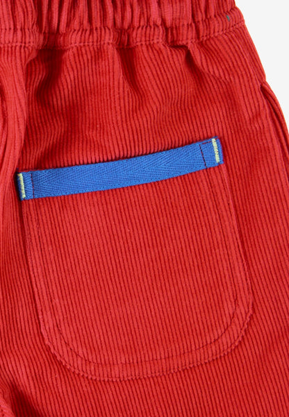 Close-up of red corduroy pants showing a front pocket with a blue fabric trim accent.